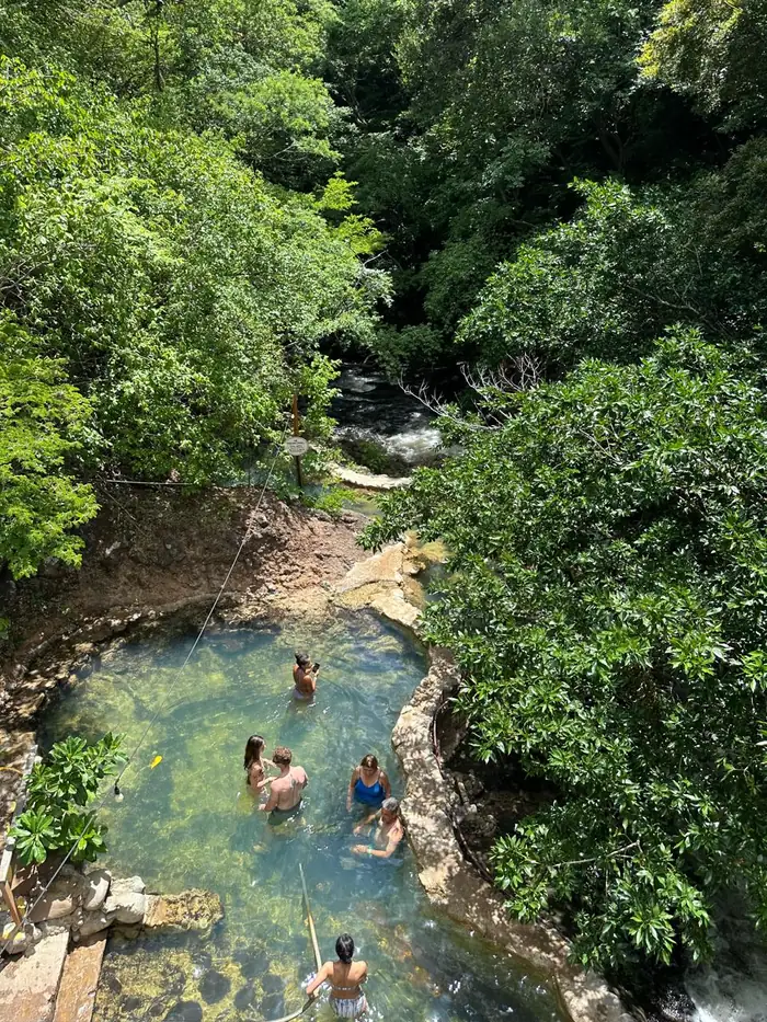 Visitors relaxing in the Rio Negro hot spring pool beneath the hanging bridge